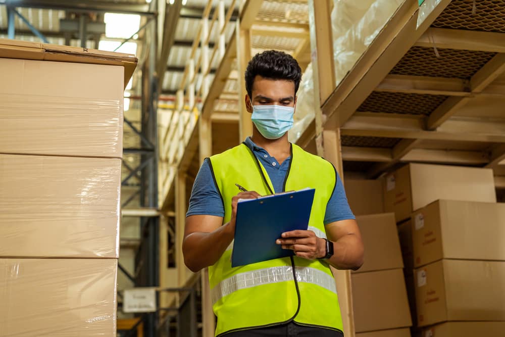 Man writing on a clipboard while standing in a warehouse full of boxes to be shipped between India and Australia as part of the free trade agreement