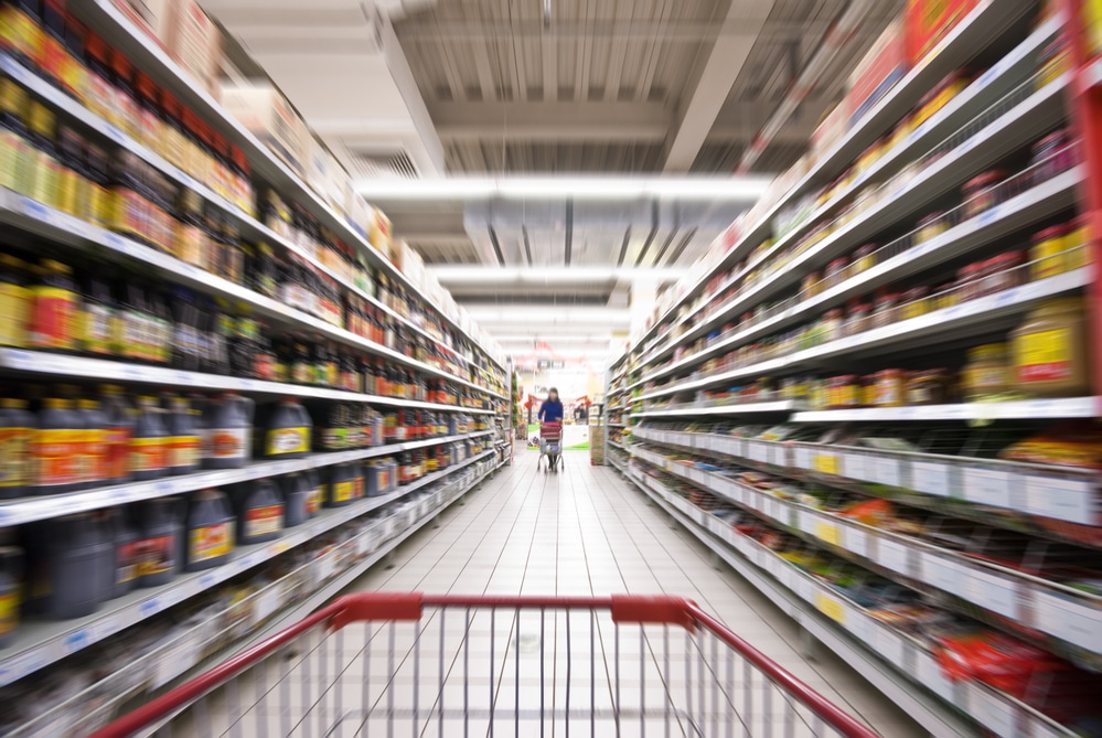 A blurred grocery aisle from the perspective of the person behind the trolley
